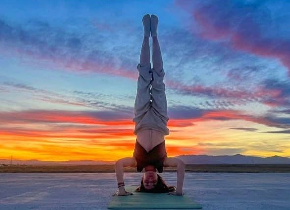 Julia in a forearm headstand on a mat in the desert under a red and orange sunset