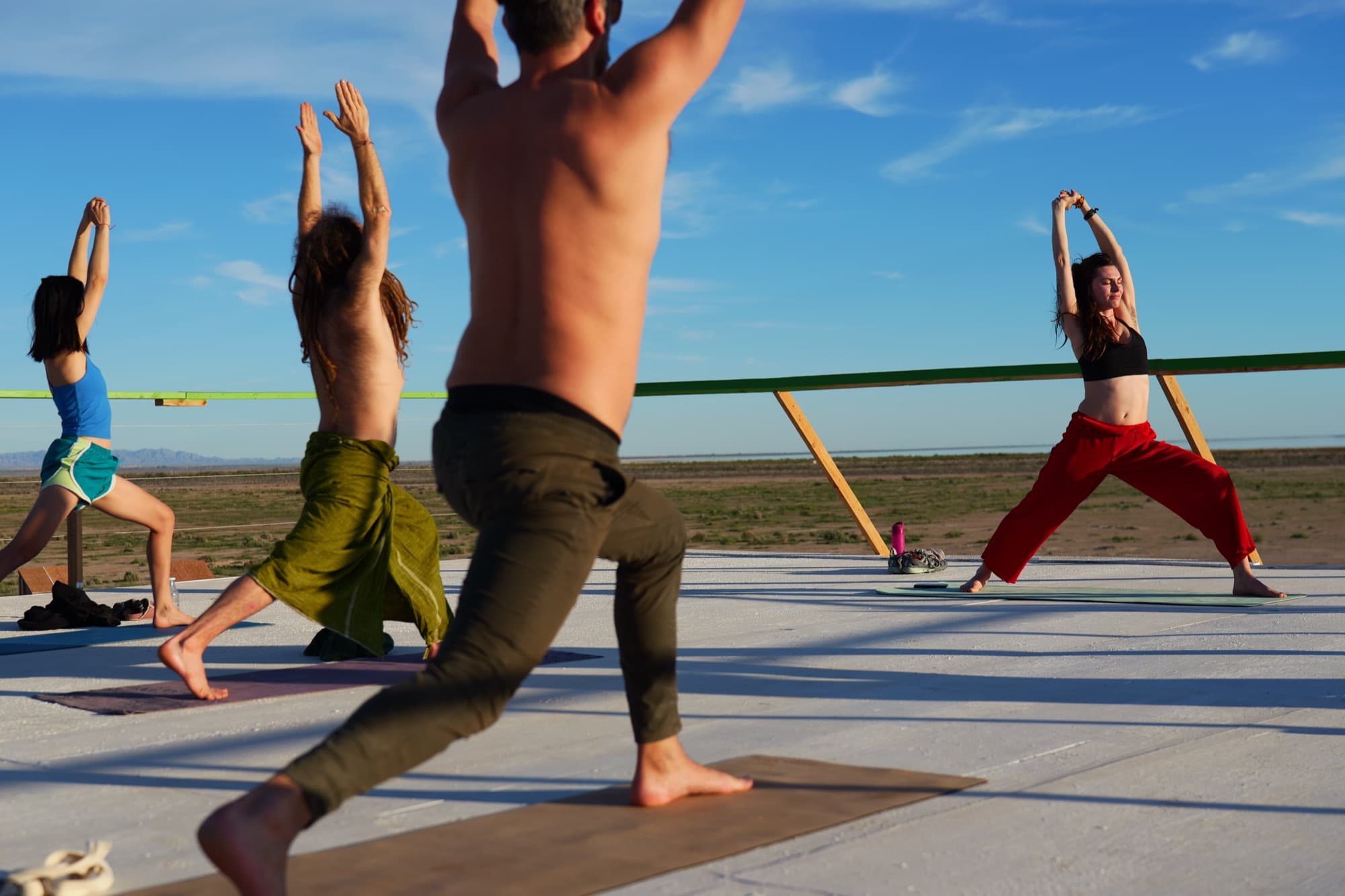 A rooftop class in warrior pose under a bright blue sky
